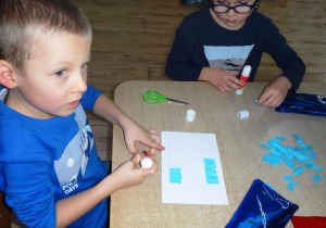 Chłopcy wyklejąją kartki klejem i papierem